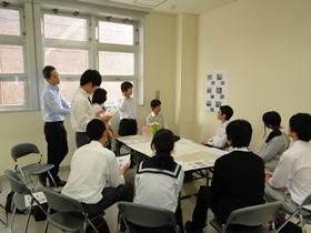 10名ほどの学生が机を囲んで数名の生徒が立って意見を発表している写真