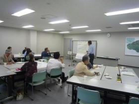 前方のホワイトボードの前に立って話をしている講師とグループごとに分かれて話を聞いている第11回管理運営ワークショップの参加者の写真