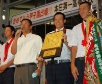 優勝旗を持って挨拶をしている本庄第一高校野球部の代表選手と監督の写真