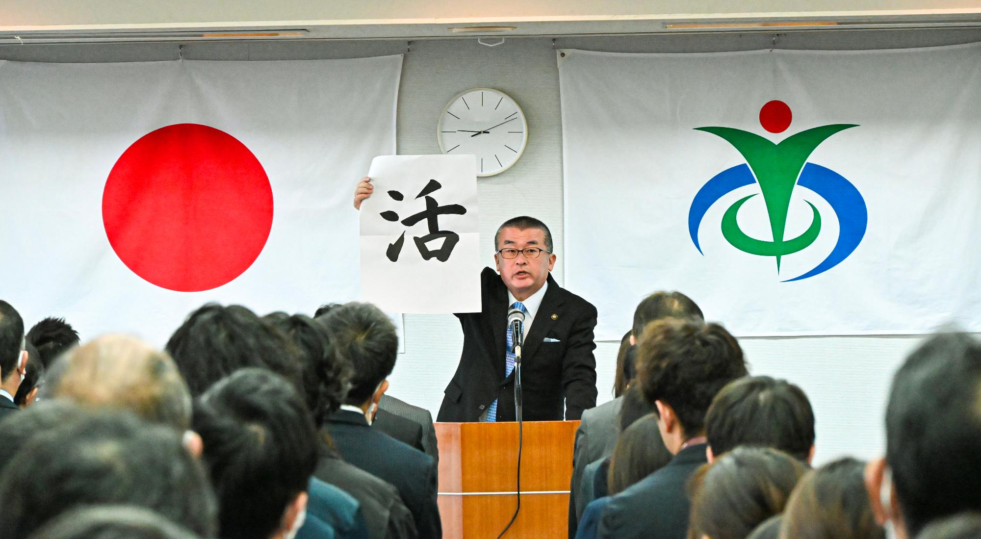 「活」という文字が書かれた半紙を掲げる本庄市長