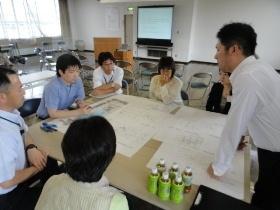 机を囲んで資料を広げワークショップをしている参加者達の写真