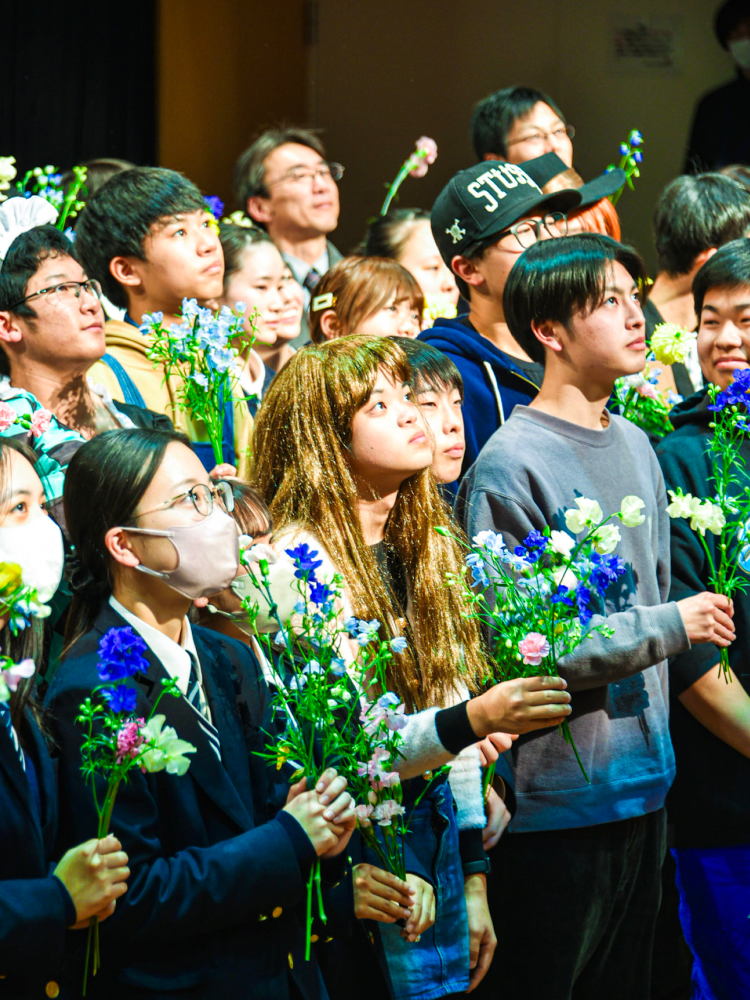 七高祭の様子、それぞれの演劇の衣装を纏った高校生たちが花を持って上を見上げている