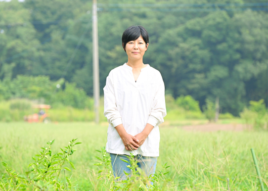 草木に囲まれた場所に立つ笑顔の女性