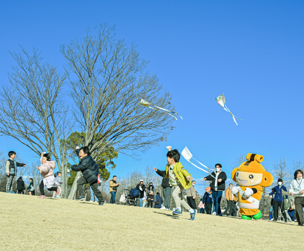 青空の下で子どもたちとはにぽんが凧揚げをして走っている
