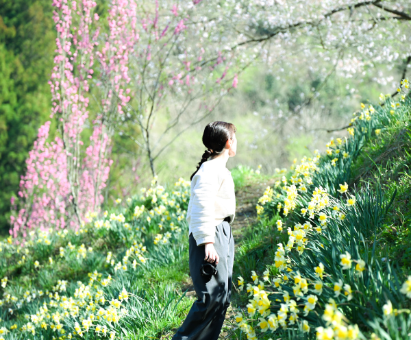 カメラを持った女性が花畑の中で後ろに振りむいている