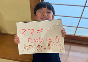 ママがたのしいまちと書かれたスケッチブックを持った幼い男の子