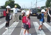 ランドセルを背負った小学生たちが右手を挙げて横断歩道を渡っている写真