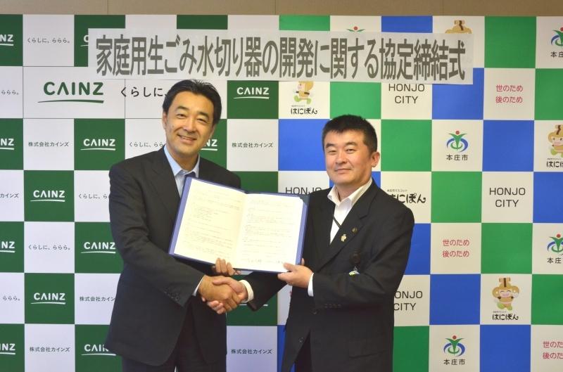 市長が土屋裕雅氏と一緒に締結書を持って握手をしている写真