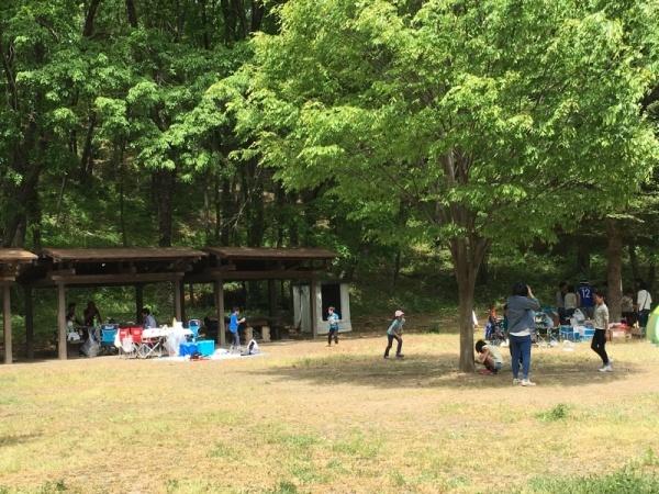 バーベキュー広場の屋根の下にある調理場にいる人たちや広場で遊んでいる子供たちの写真