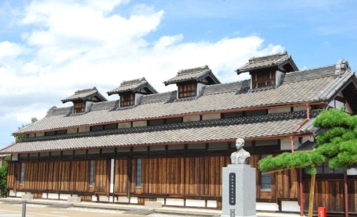 木造2層建築の競進社模範蚕室の前に木村九蔵の銅像がある写真