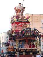 神功皇后の人形が上にたっており、袴を着た4人の人たちが中央に座っている本庄上町の山車の写真