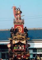 神功皇后の人形が乗っておりその下の屋根に3名の大人が立ち中央にも3名の人が座っている児玉仲町の山車の写真