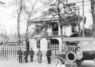 警察官や袴を着た人や古い車が写っている昭和2年頃の本庄警察署の白黒写真