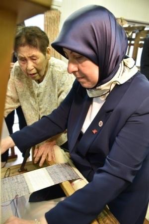 高齢女性の指導で織物体験をしている夫人の写真