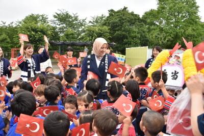 トルコの国旗を持った園児たちが婦人の周りを囲んでいる写真