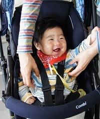 ベビーカーに乗ってお母さんの手につかまり笑顔の赤ちゃんの写真