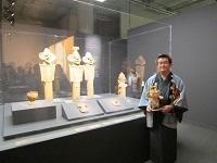 「笑う盾持人物埴輪」3体の展示の前ではにぽんを縮小した人形を持っている袴姿の市長の写真