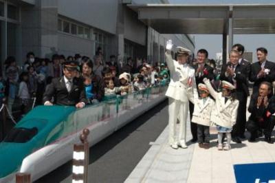本庄早稲田駅開業10周年記念式典にて白いジャケットと帽子を被った駅員さんと子供たちがはやぶさの乗り物に乗った参加者たちを見送っている写真