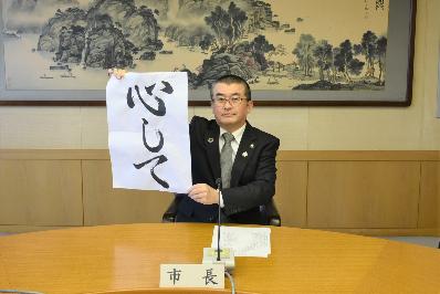 「心して」という文字が書かれた半紙を掲げる本庄市長