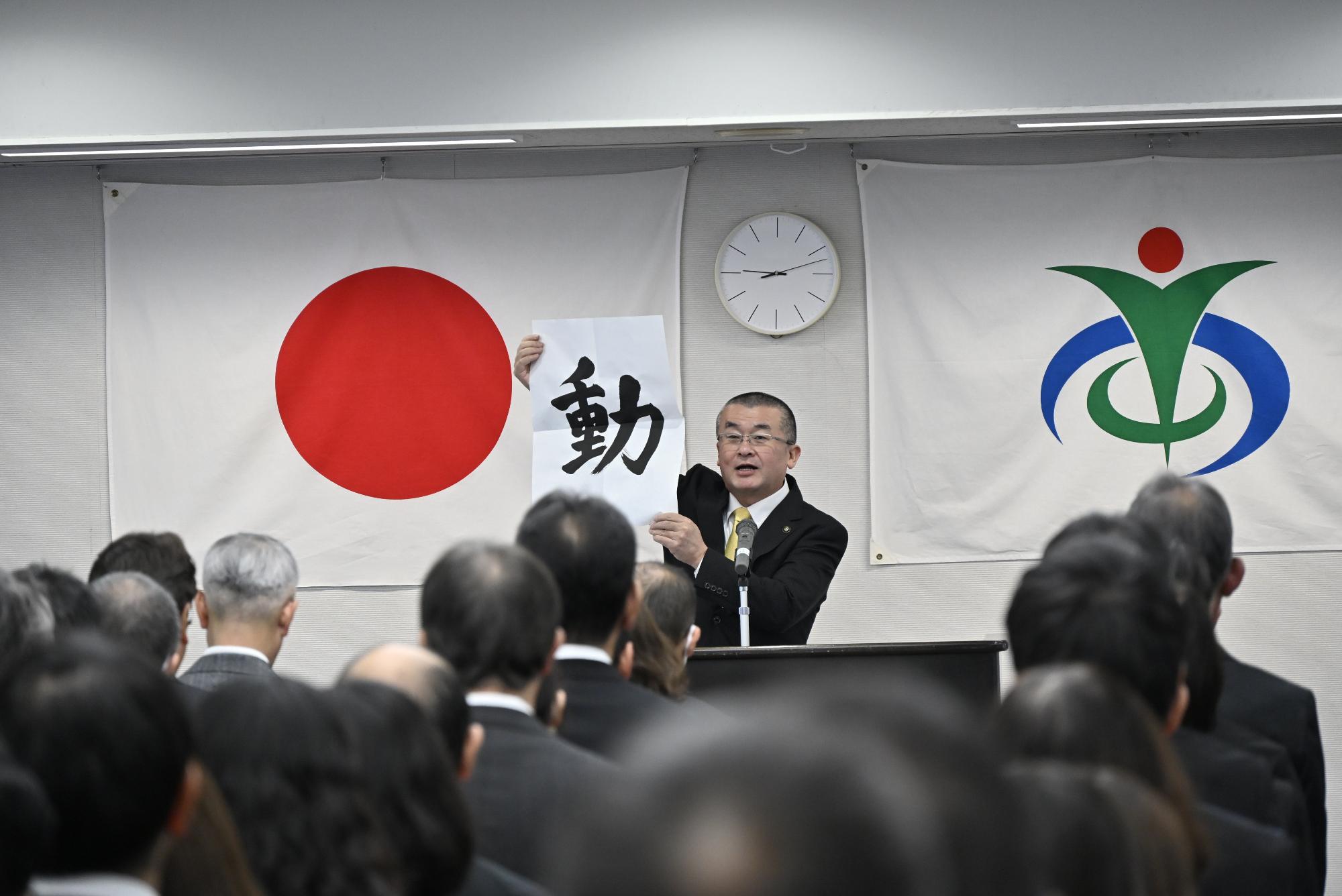 「動」という文字が書かれた半紙を掲げる本庄市長